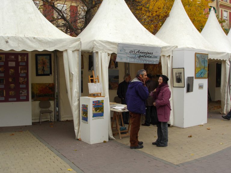 Carpas de una feria de arte al aire libre con cuadros expuestos y gente conversando.