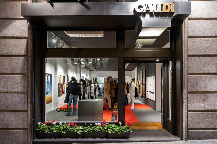 Escaparate y entrada de la Galería Gaudí con alfombra roja y gente dentro mirando obras.
