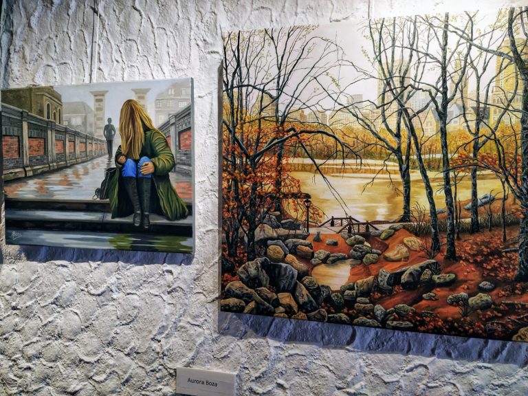 Dos cuadros colgados en una pared de piedra con una cartela con el nombre de la artista.